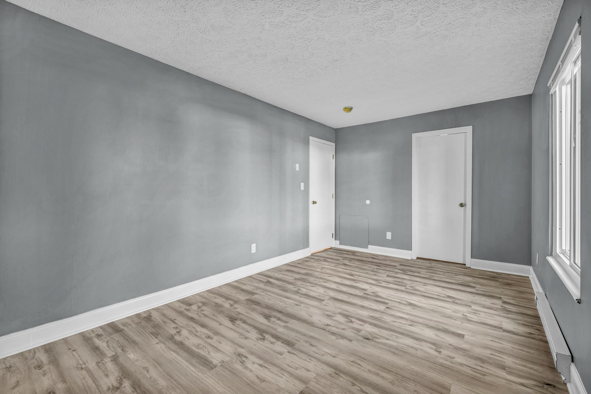Empty rental room with grey walls, white doors and light wood flooring, ready for a move-out walkthrough.