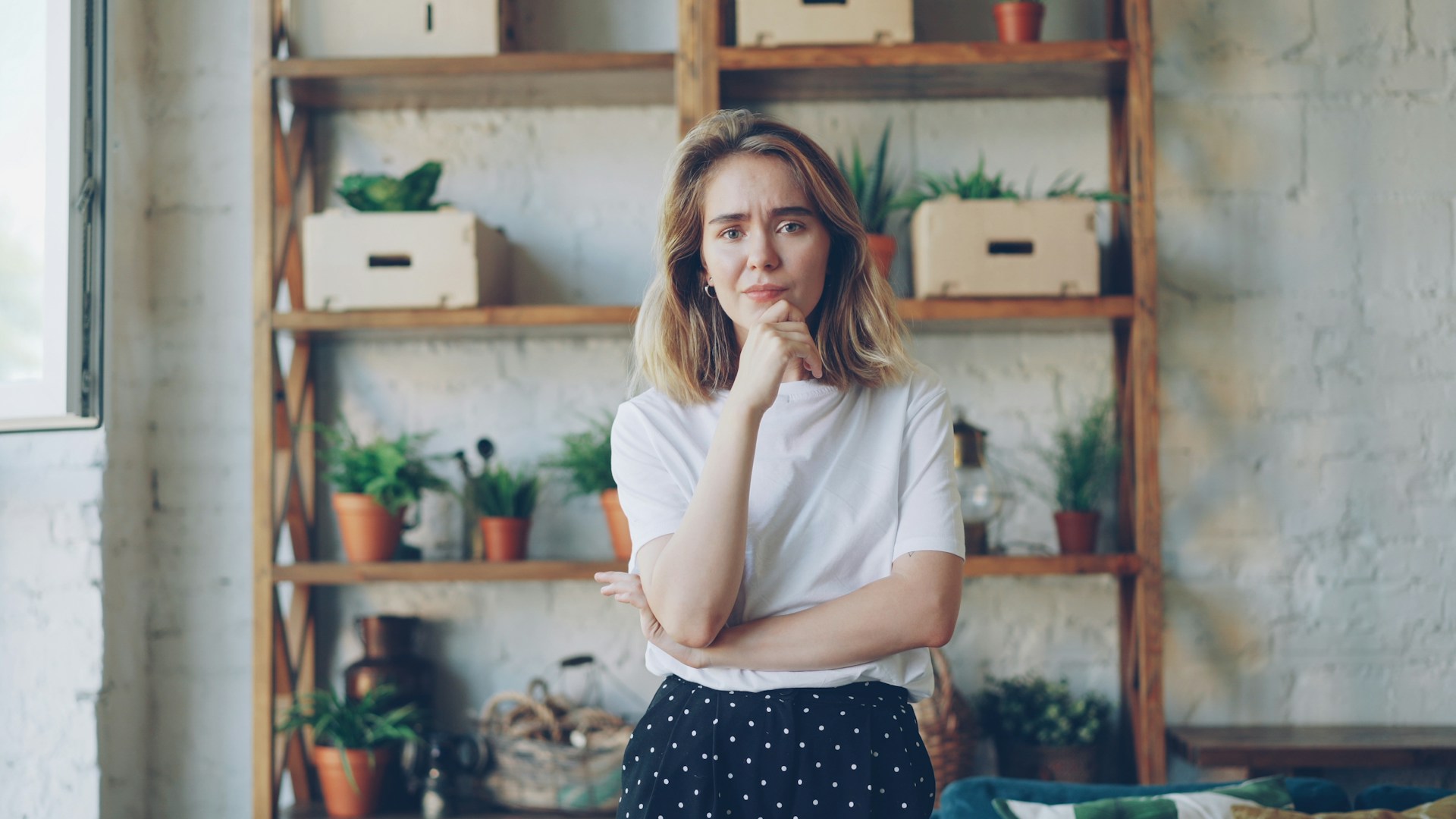 Woman standing in front of wooden shelving unit displaying home décor items and storage containers.