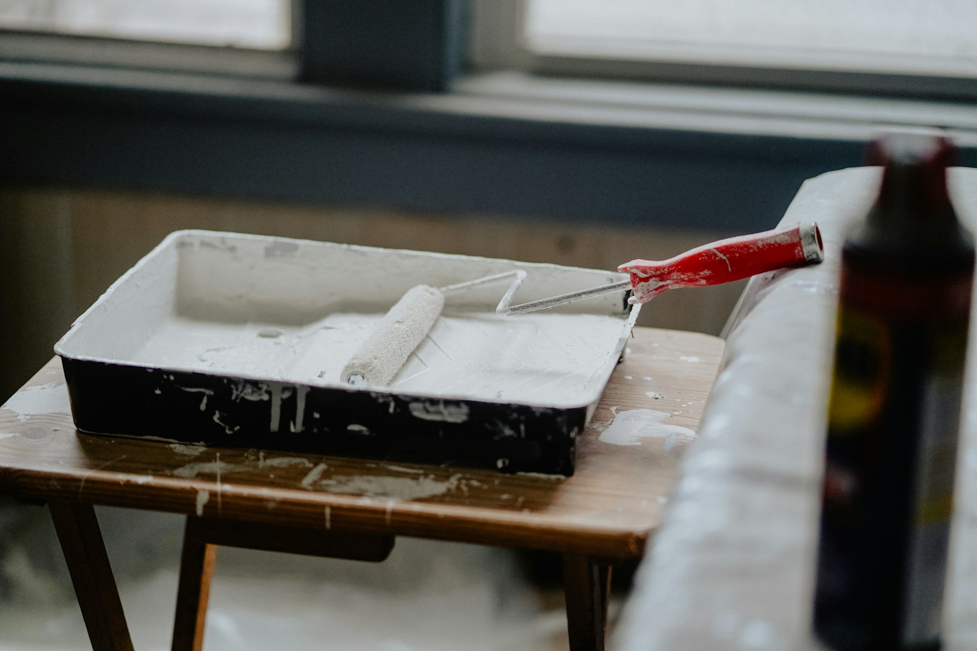 Paint roller resting in a tray of white paint during a rental unit repair.